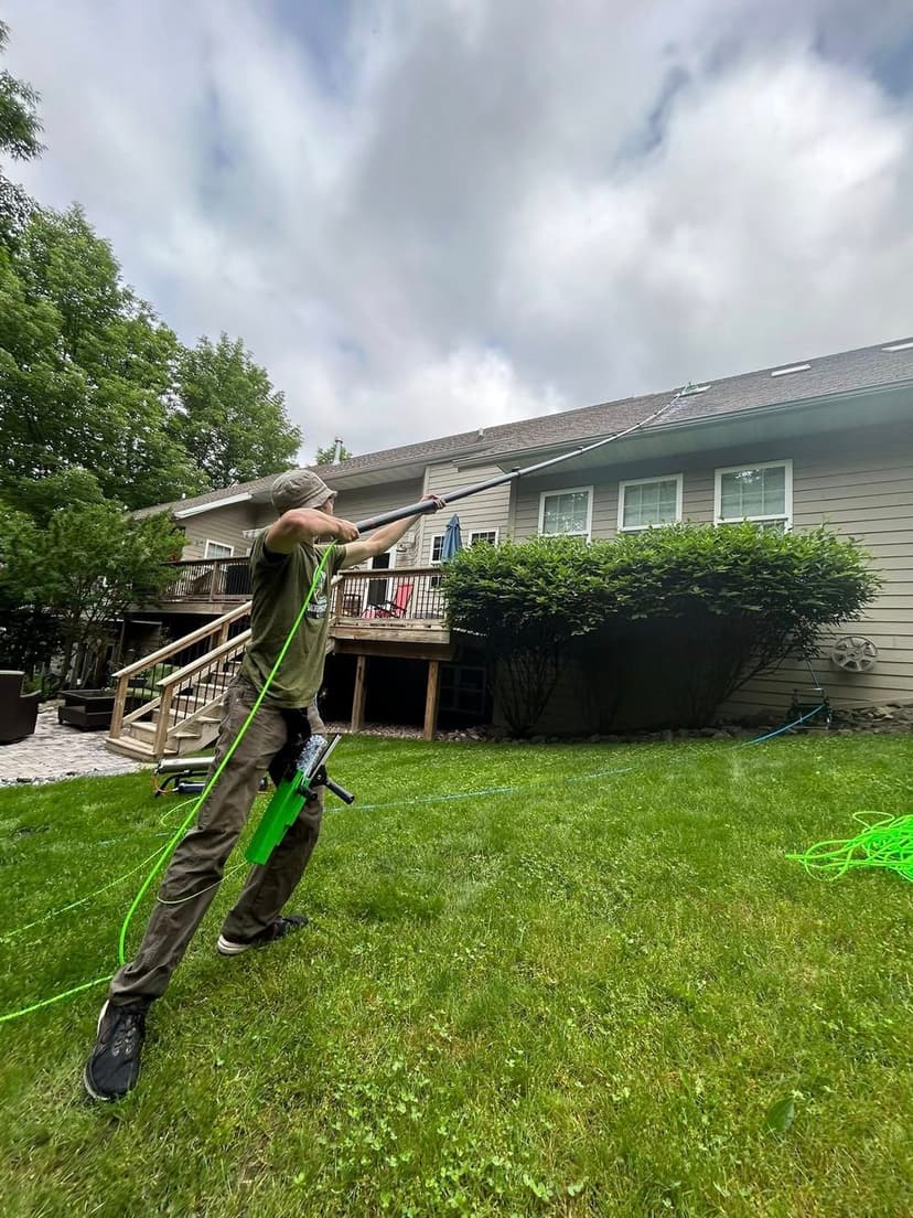 Person using a power washer with green hose in backyard, cloudy sky above.